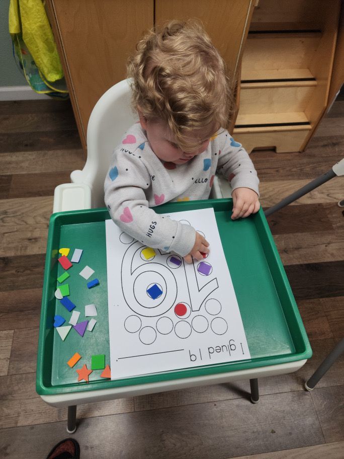 A little girl is sitting in a high chair drawing on a piece of paper