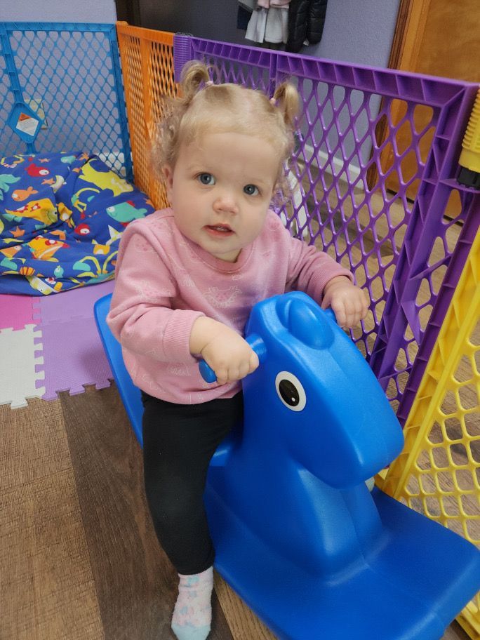 A little girl is sitting on a blue rocking horse