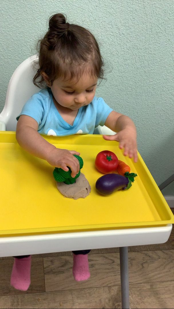 A little girl is sitting in a high chair playing with play dough.