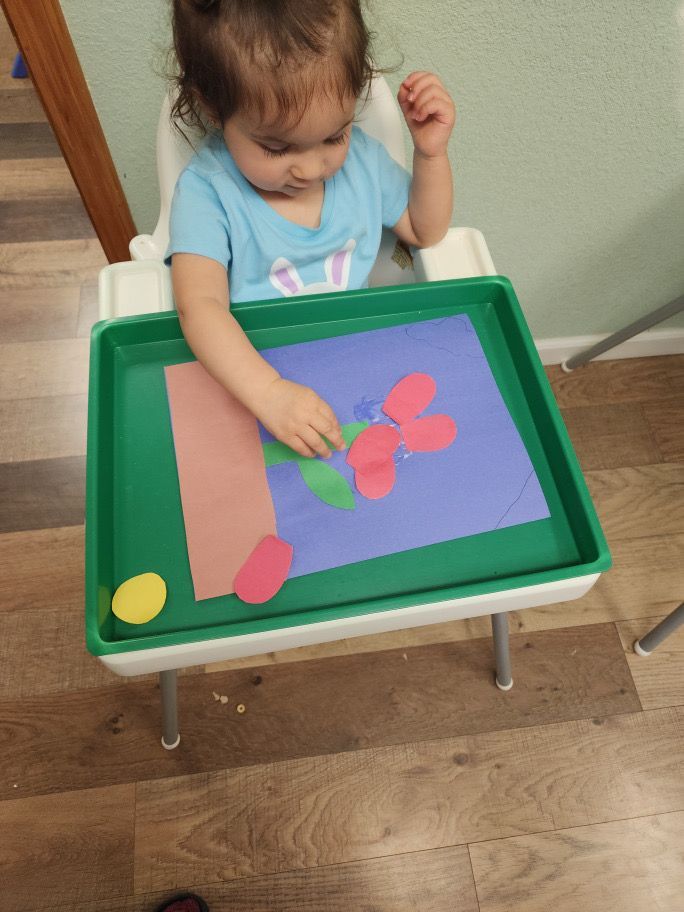A little girl is sitting in a high chair playing with paper