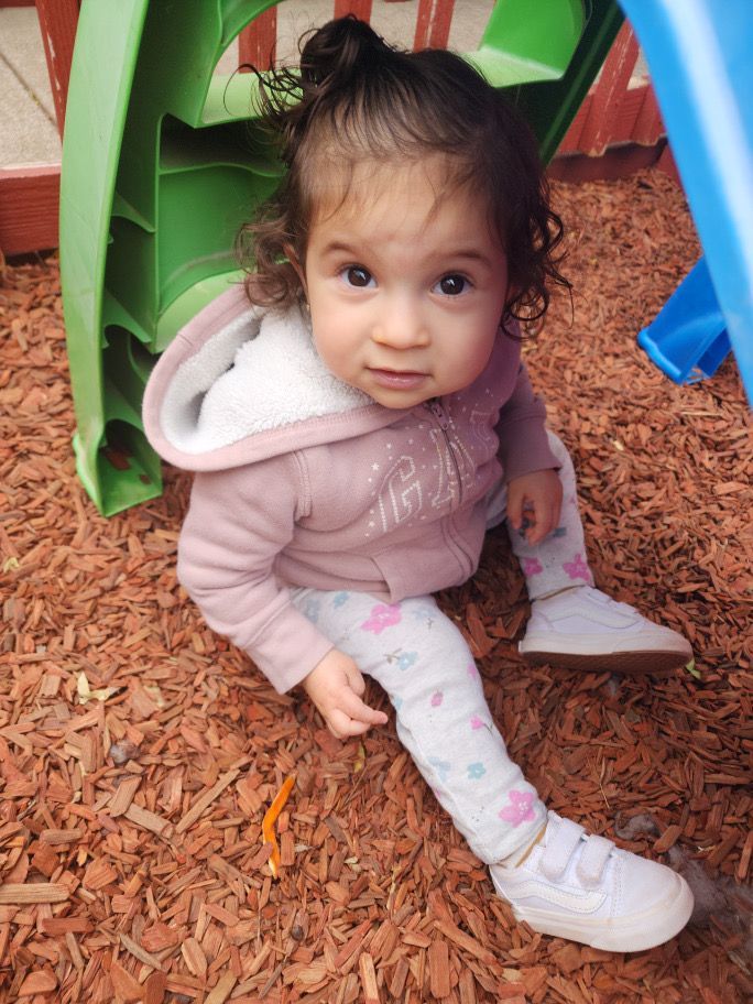 A little girl is sitting on the ground in front of a green slide