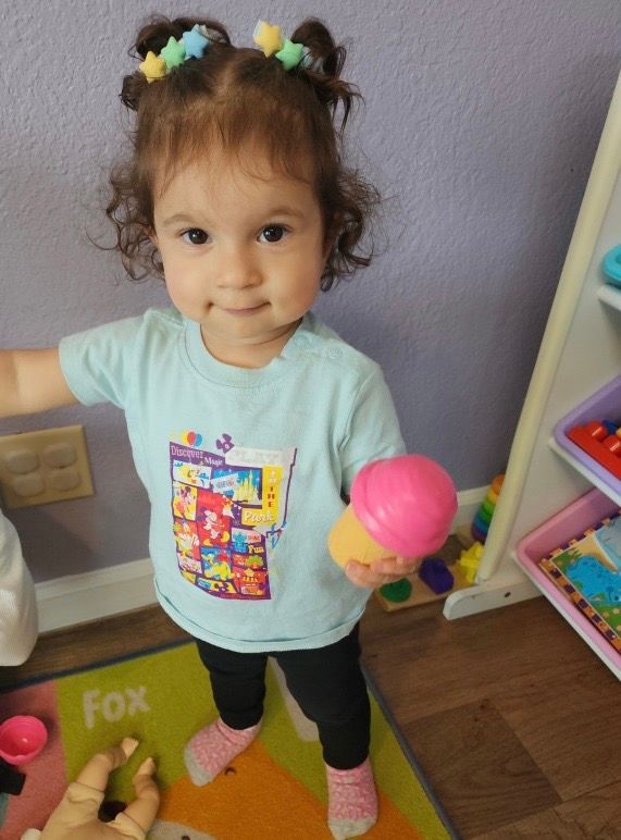 A little girl is holding a pink toy ice cream cone.