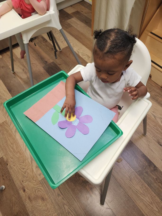A little girl is sitting in a high chair playing with a paper flower