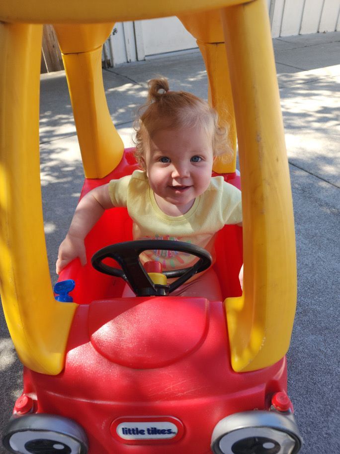 A little girl is sitting in a little tikes toy car