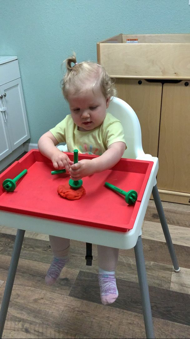 A little girl is sitting in a high chair playing with play dough