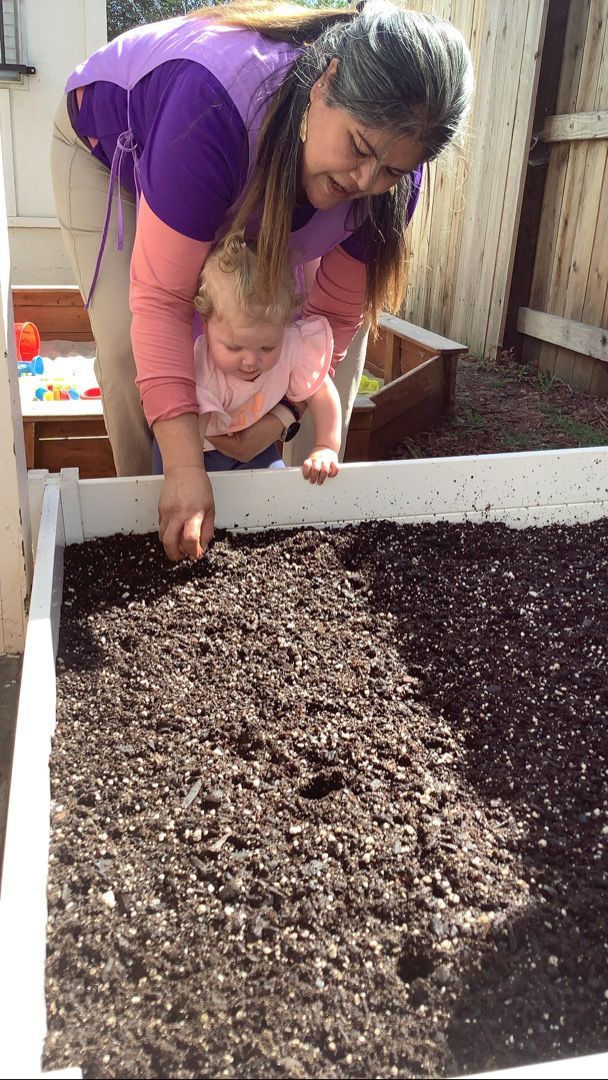 A woman is holding a baby in her arms and they are playing with dirt