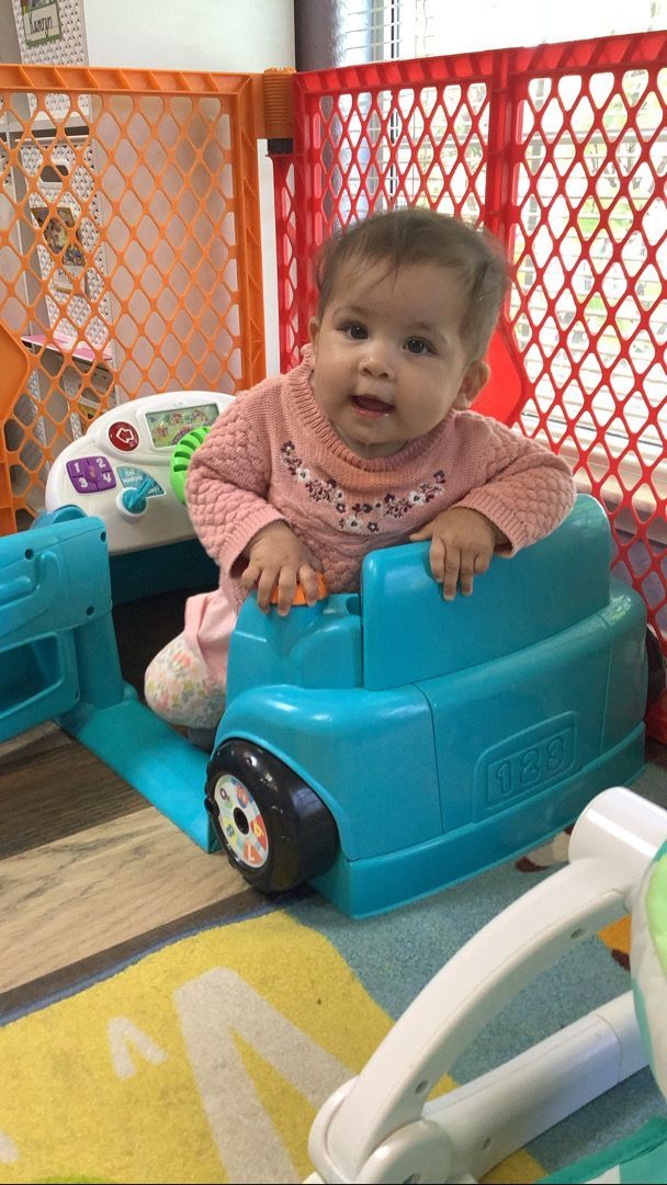 A baby is sitting on a toy car in a room.