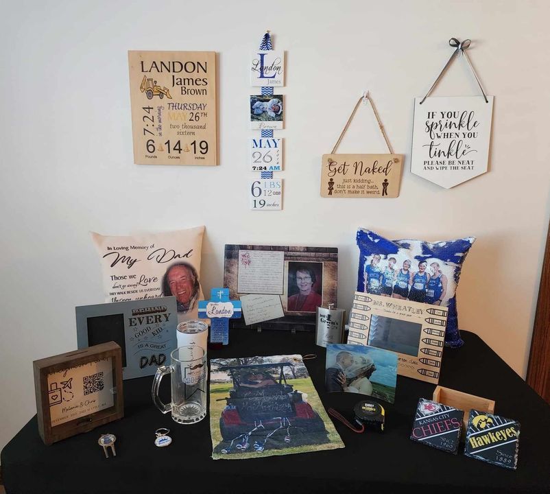 Memorial items on table: photos, signs, pillows, and a tumbler.