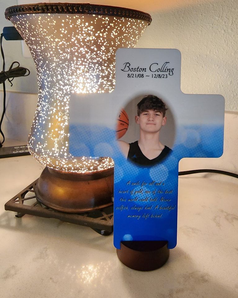 A cross-shaped memorial with a photo of a young person holding a basketball. It's in front of a lit, decorative lamp.