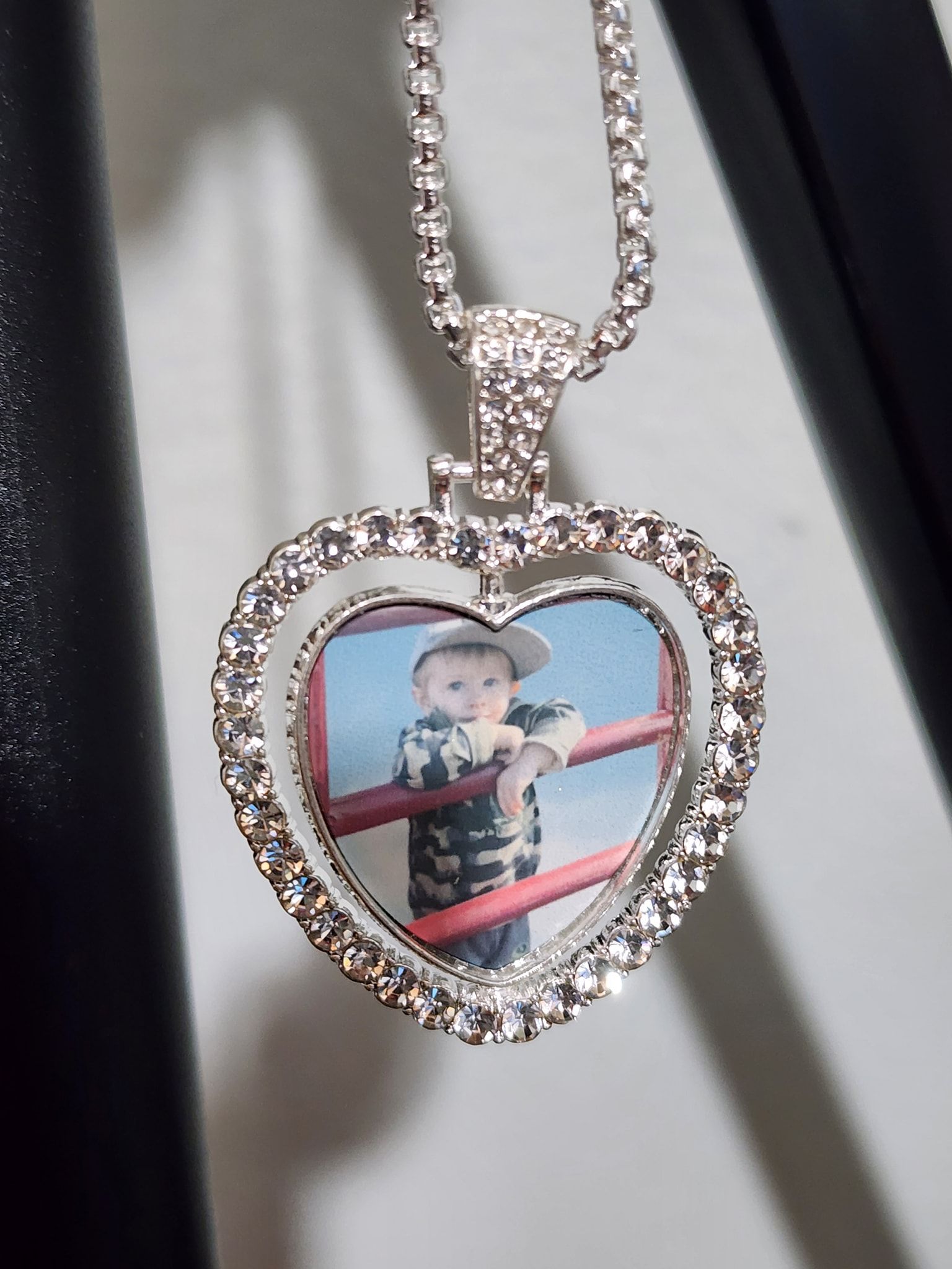 Heart-shaped pendant necklace with small photo of a boy in front of a fence, surrounded by rhinestones.