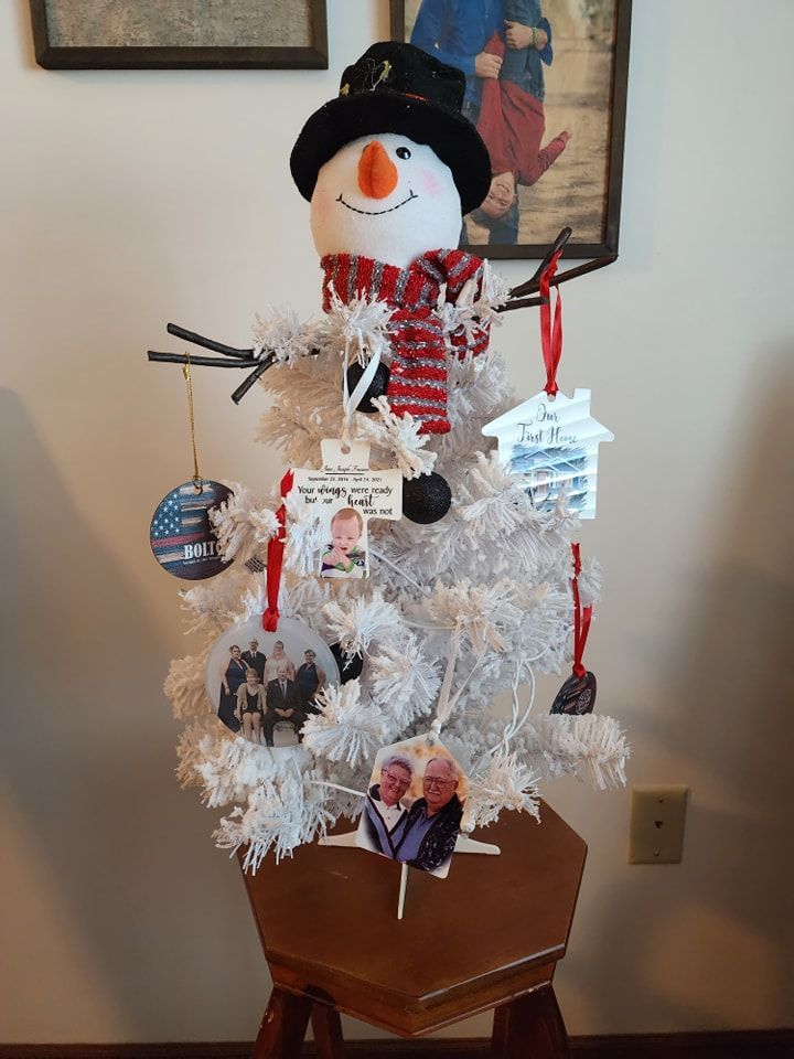 White snowman tree decorated with ornaments on a small wooden stool, with pictures in the background.
