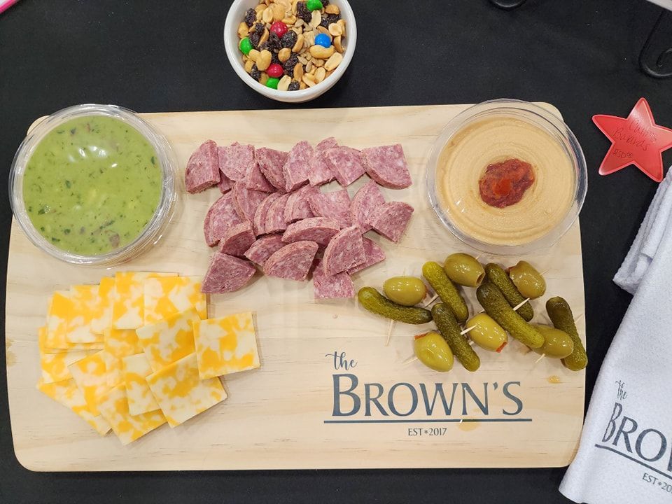 Charcuterie board with salami, cheese, dips, olives, pickles, and snack mix.
