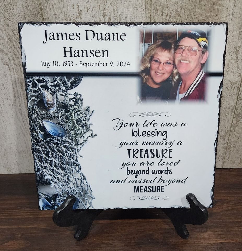 Memorial plaque with a photo of a couple, name, dates, and inscription, displayed on a stand.