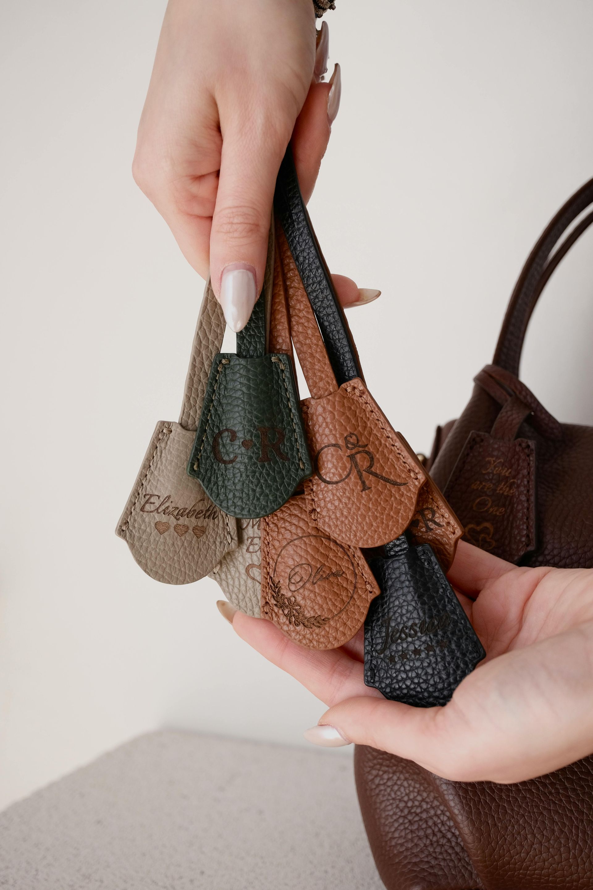 Hands holding a variety of leather bag charms in different colors.