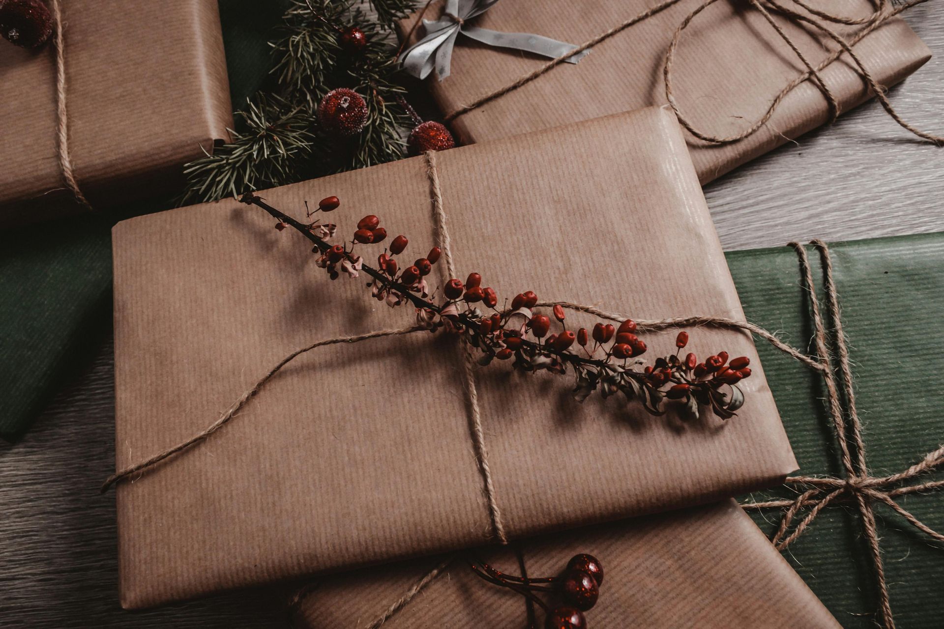 Wrapped gifts in brown and green paper, tied with twine and decorated with berries and greenery.