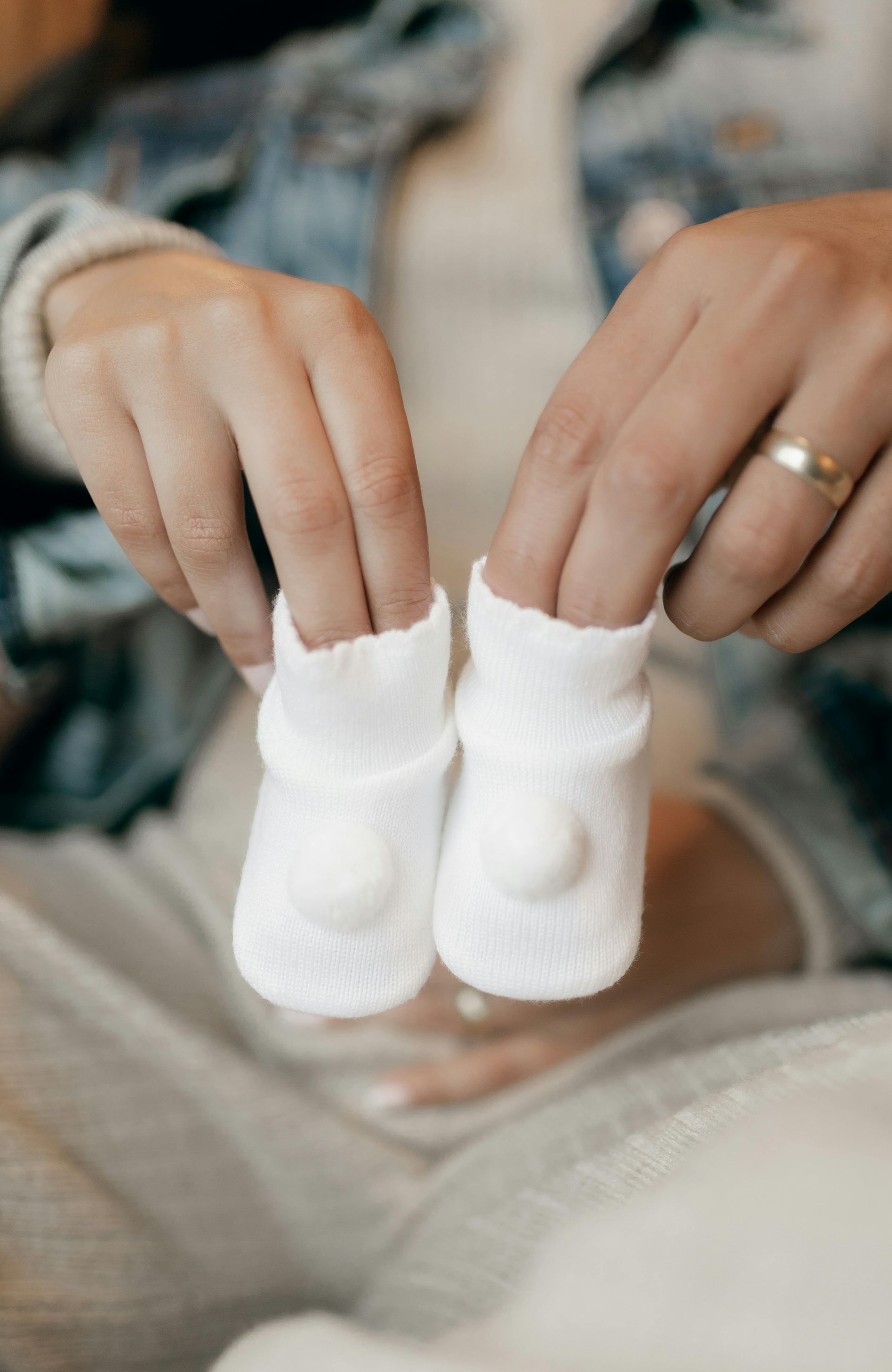 Person holding two small white baby booties in front of a pregnant belly.