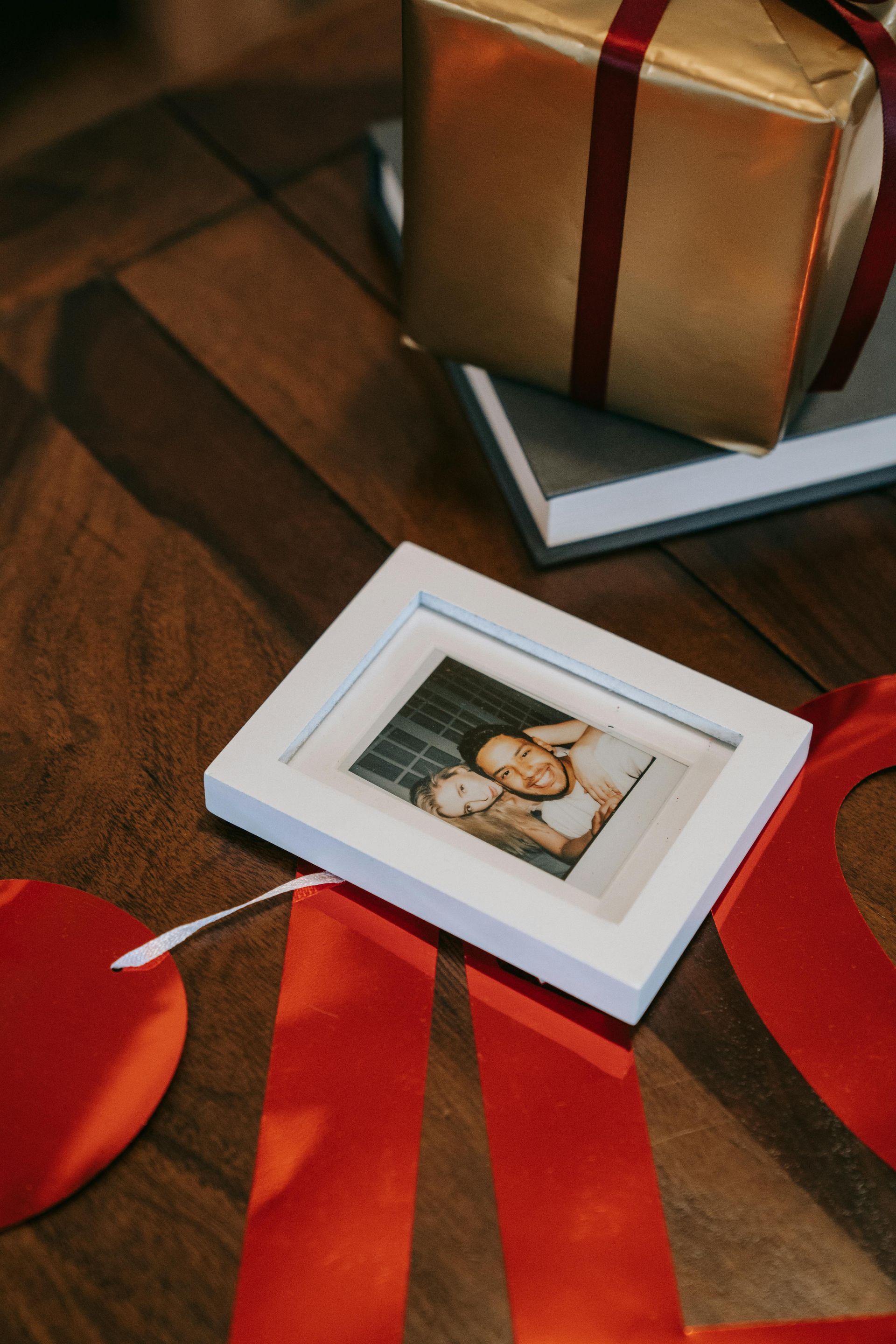 Gift box, framed photo, and red ribbon on a wooden surface, suggesting a celebration.