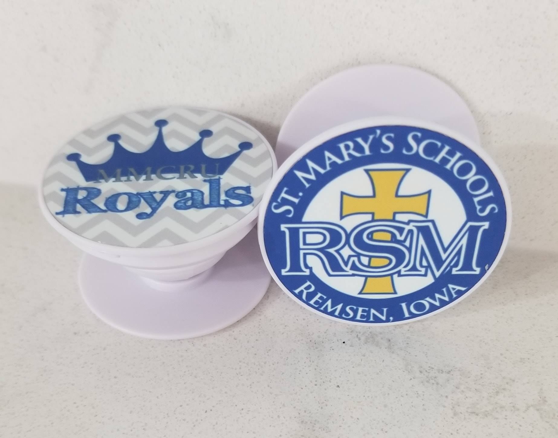 Two pop sockets with school logos: MMC RU Royals and St. Mary's Schools RSM Remsen, Iowa.