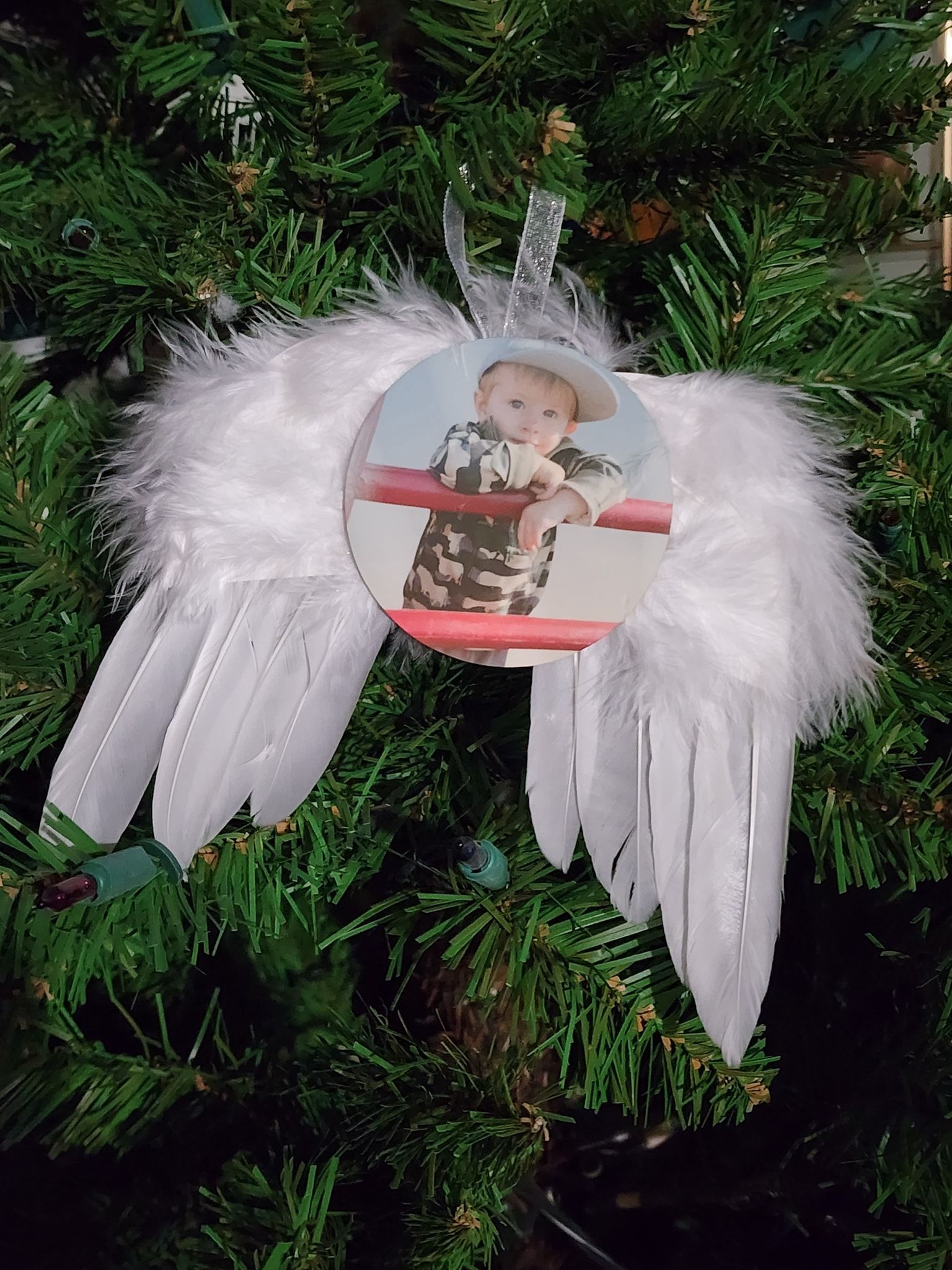 Christmas ornament: a child's photo in a circle, surrounded by white feather angel wings, hanging on a Christmas tree.