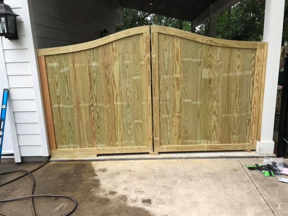 A wooden gate is sitting on top of a concrete driveway next to a house.