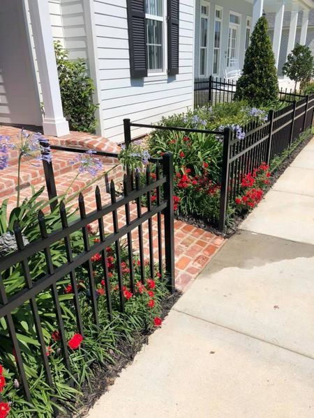 A black fence surrounds a brick walkway in front of a house.