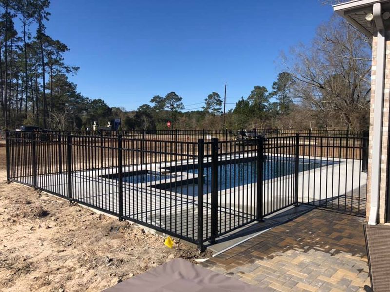 A black fence surrounds a swimming pool in a backyard.