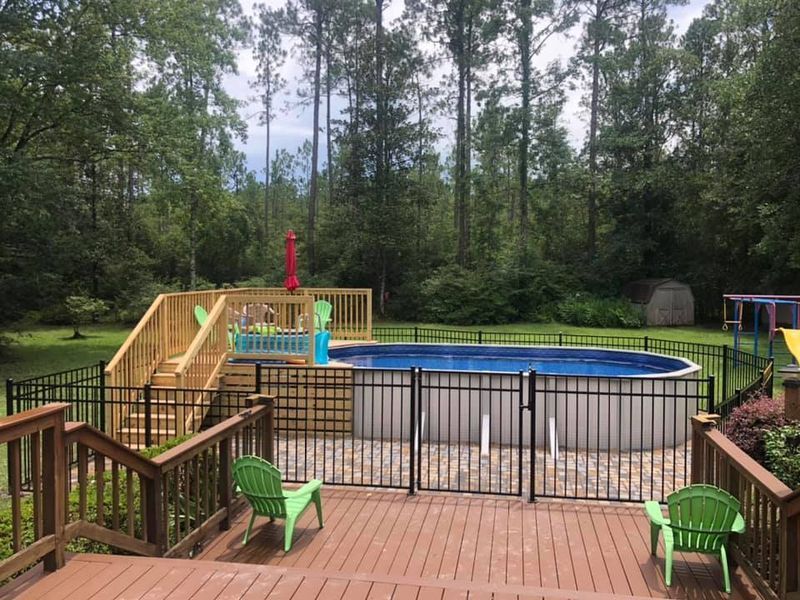 A large swimming pool is surrounded by a fence and a wooden deck.