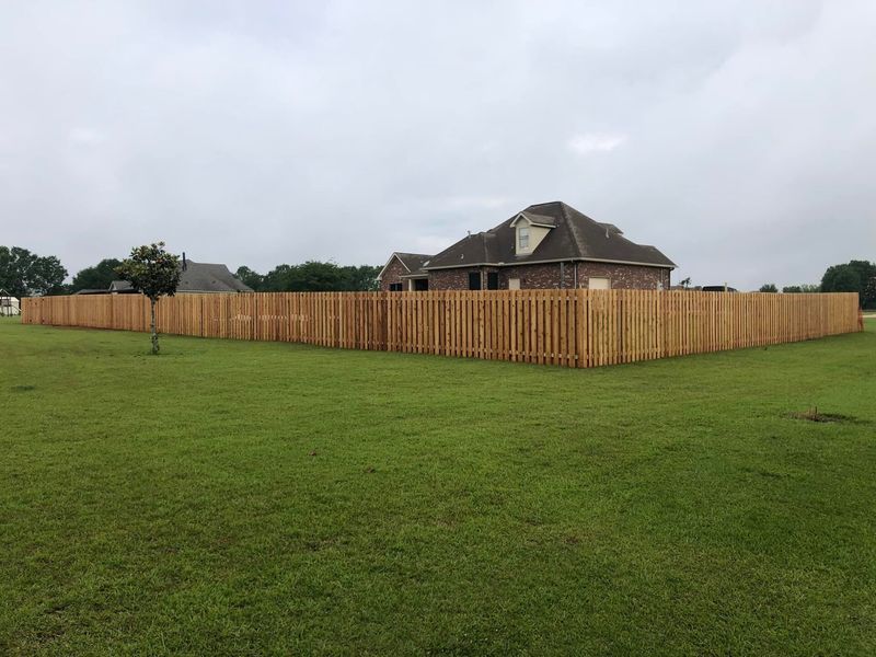 A wooden fence surrounds a lush green field in front of a house.