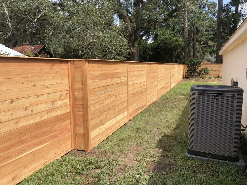 A long wooden fence is in the backyard of a house.