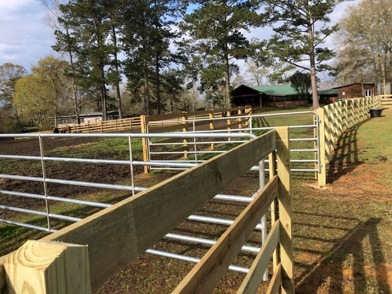 A wooden fence with metal bars is surrounded by grass and trees.