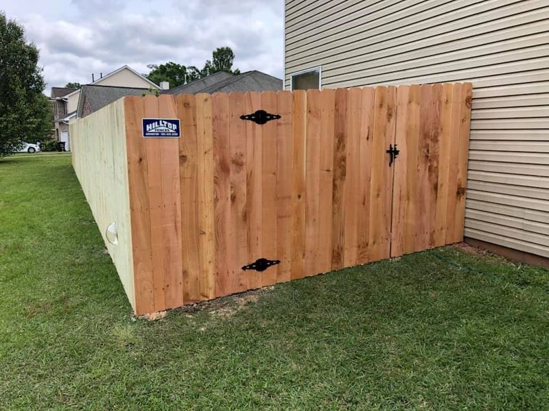 A wooden fence is sitting in the grass next to a house.