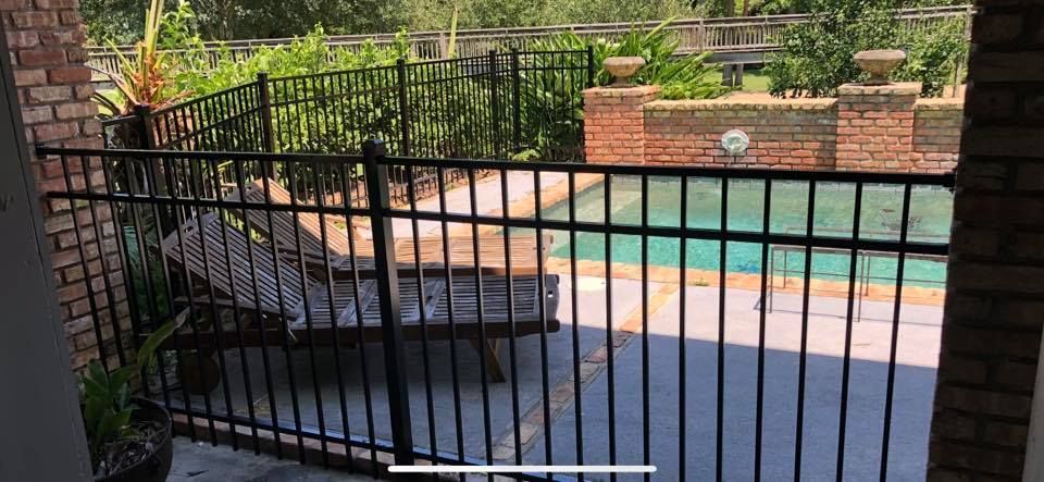 A black fence surrounds a patio area with a pool in the background.