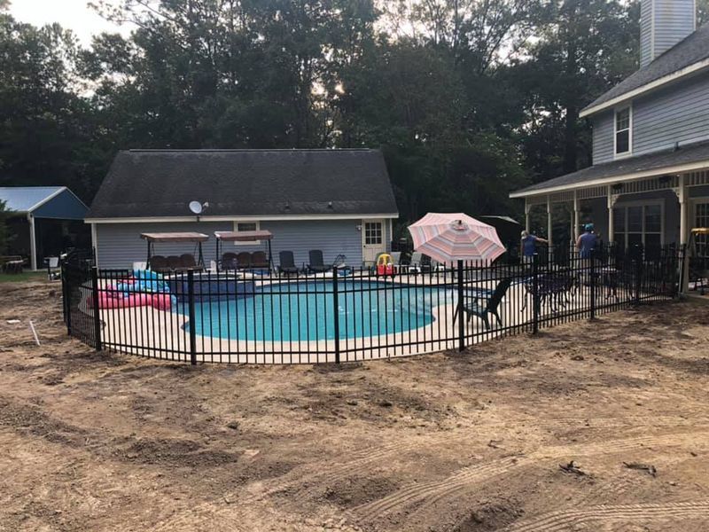 A large swimming pool surrounded by a metal fence in front of a house.
