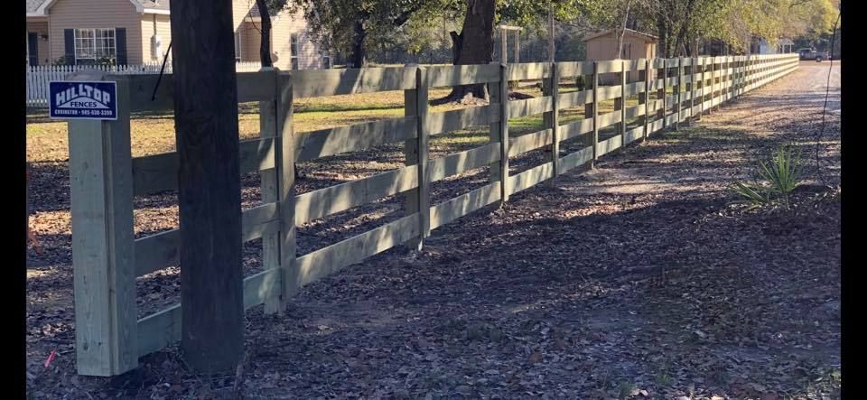A wooden fence surrounds a dirt road in front of a house.