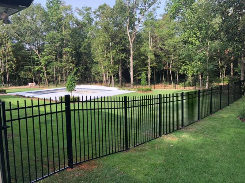 A black fence surrounds a lush green yard with a pool in the background.