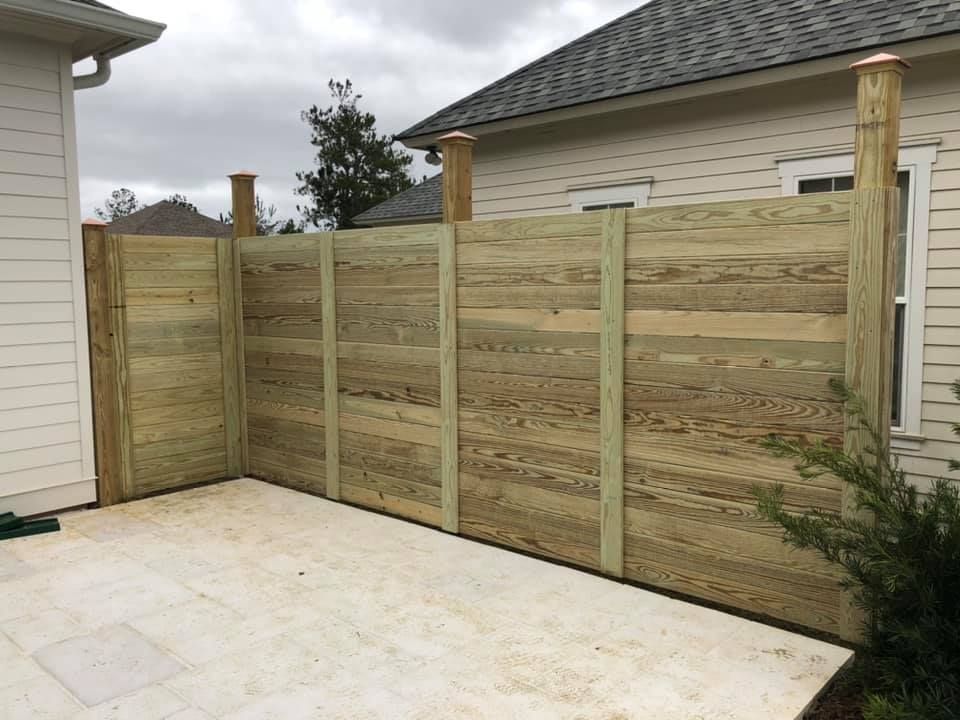 A wooden fence is surrounding a patio in front of a house.