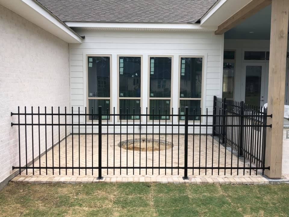 A black fence surrounds a patio with a fire pit in the middle of it.