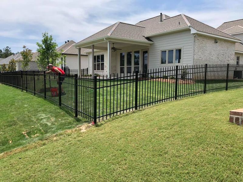 A black fence surrounds a large lawn in front of a house.