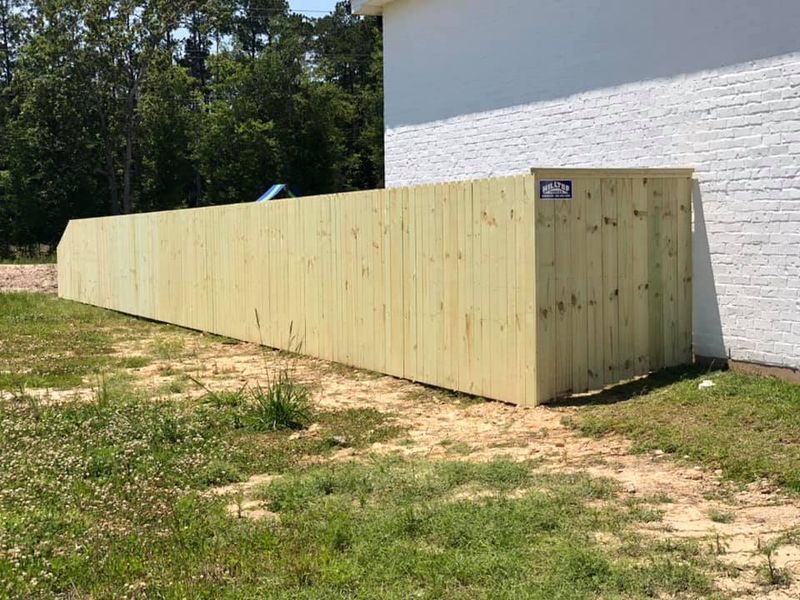 A wooden fence is sitting in the grass next to a white brick building.