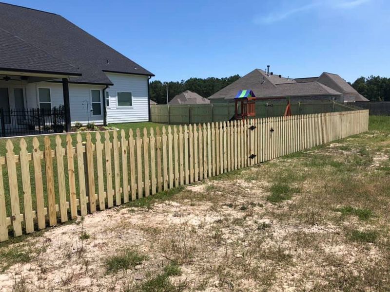 A wooden picket fence is in the backyard of a house.