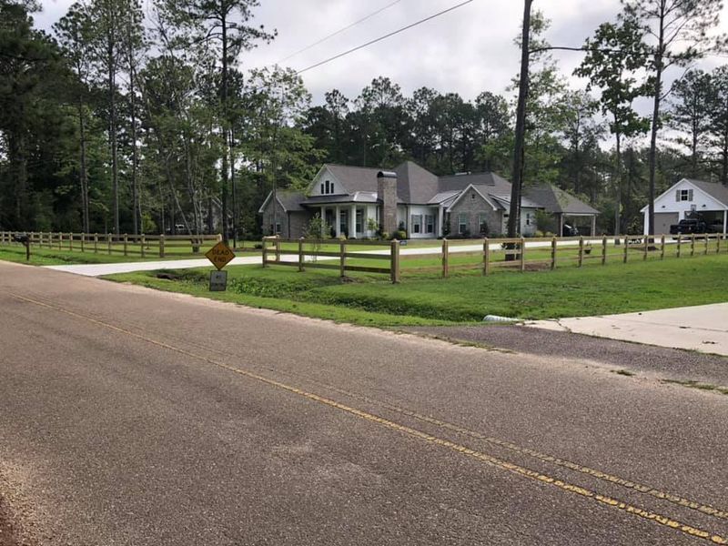 A large house sits on the side of a road surrounded by trees