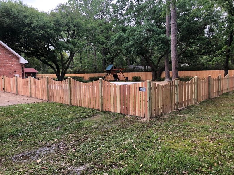 A wooden fence surrounds a swimming pool in a backyard.
