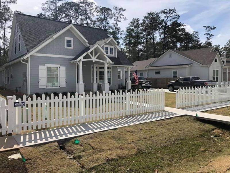 A gray house with a white picket fence in front of it