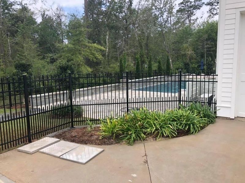 A black fence surrounds a swimming pool in a backyard.