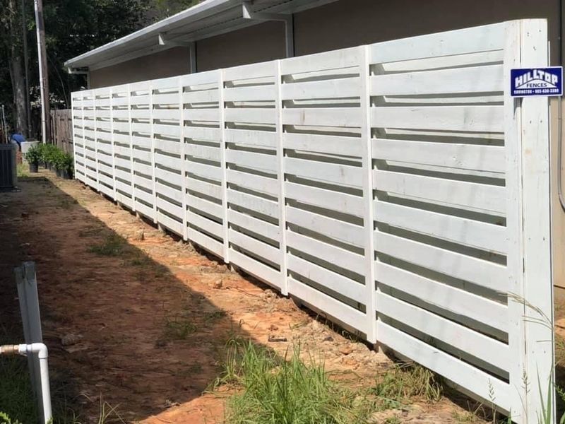 A white wooden fence is sitting next to a house.
