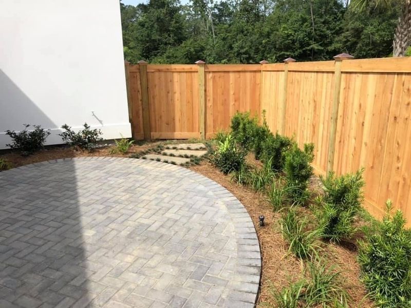 A wooden fence surrounds a patio with a brick walkway.