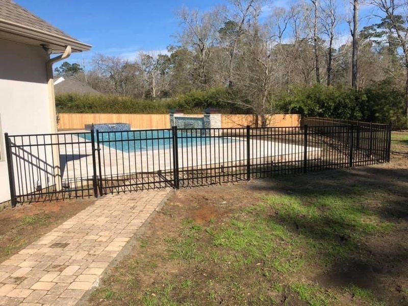 A black fence surrounds a swimming pool in a backyard.