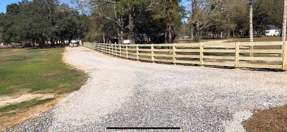 A gravel road with a wooden fence along the side of it.
