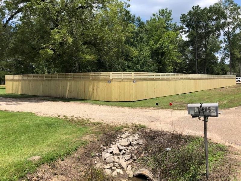 A large wooden fence is surrounded by trees and a mailbox.