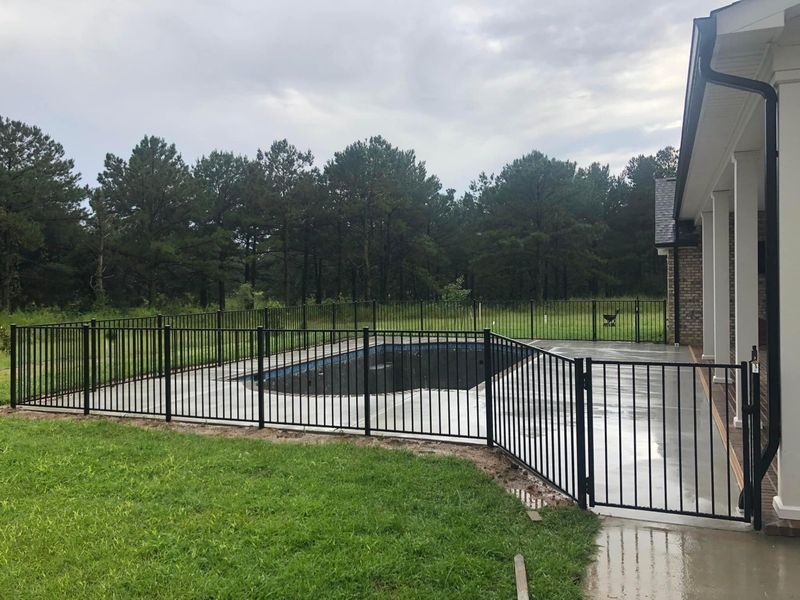 A fence surrounds a swimming pool in the backyard of a house.